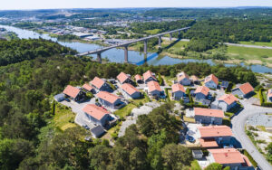 Flygbild över bostadsområde med småhus framför bro över älv.
