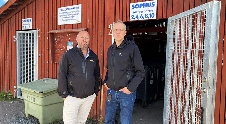 Två allvarliga män står utanför en röd byggnad